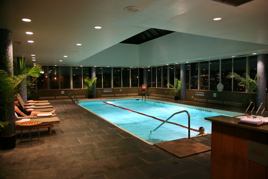 Piscine intérieure éclairée, transats, vue nocturne ville.